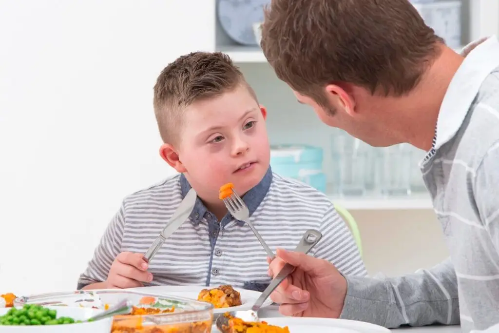 Junge mit Trisomie 21 isst gemeinsam mit Mann